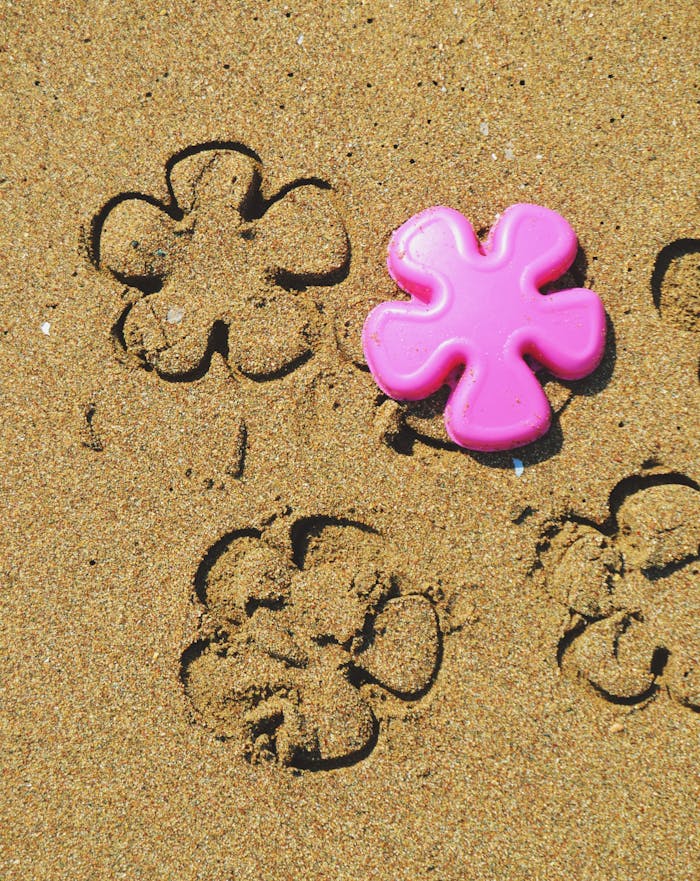 Close-up of a pink plastic flower toy creating imprints on a sandy beach.